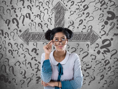 Thoughtful businesswoman in front of wall with arrow symbol and question marks