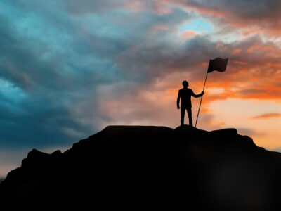 business, success, leadership, achievement and people concept - silhouette of businessman with flag on mountain top over sunset background